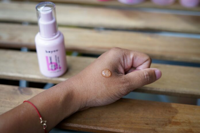 Photo by Alexandra Tran a woman's hand holding a bottle of sunscreen on a wooden bench